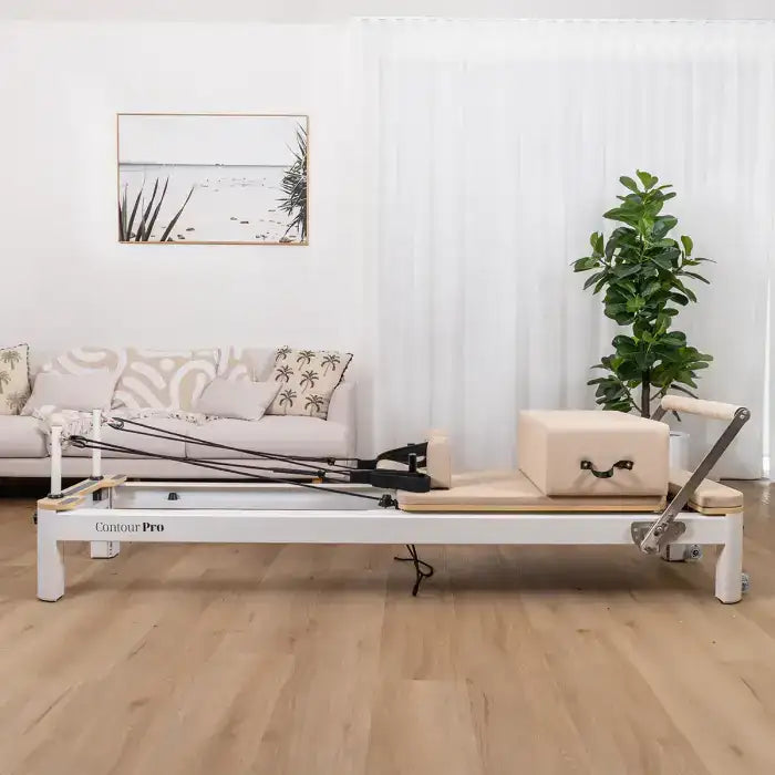 White pilates reformer with black and silver resistance bands, wooden platform, and metal frame.