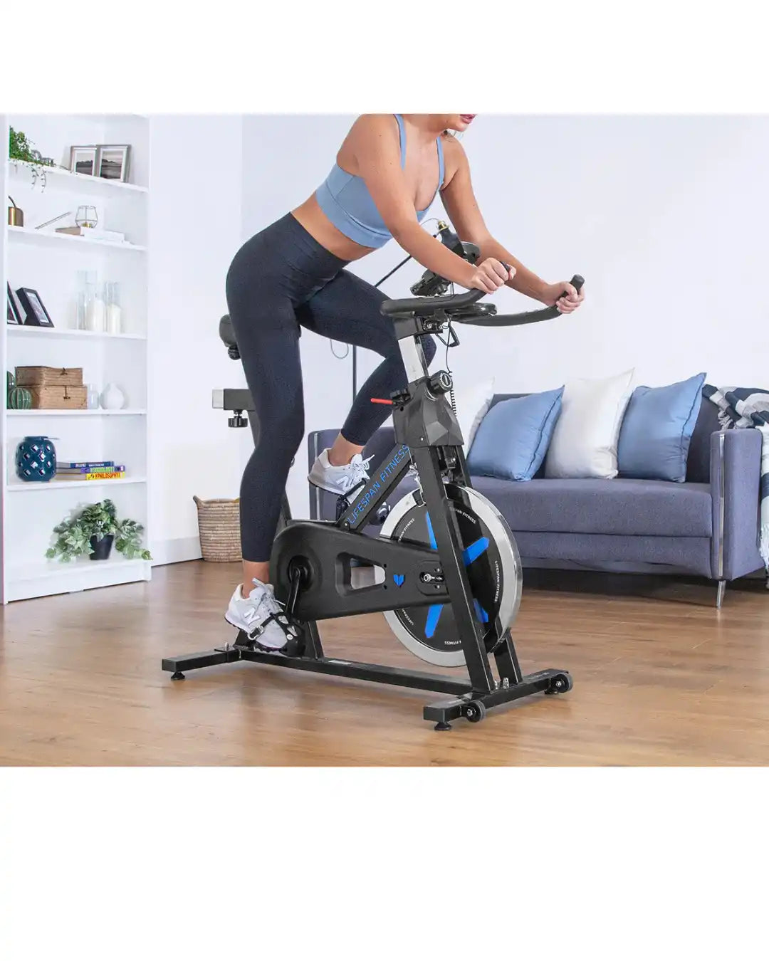 A woman on a stationary exercise bike with a black frame and blue accents.